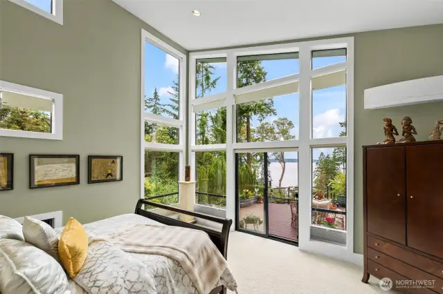 The primary suite is a private sanctuary with soaring ceilings and a dramatic wall of windows that frame tranquil water views and open directly to the main deck.