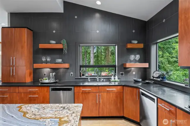 This architecturally striking kitchen is both a visual centerpiece and a culinary workspace. Bold tile, slab granite, floating shelves, and windows that frame the forest make this space feel grounded, sophisticated, and deeply connected to its natural surroundings.