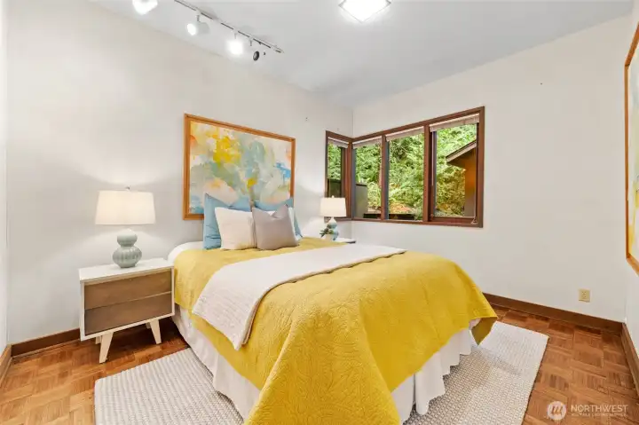 Bedroom Two: Bright and welcoming with parquet flooring, generous natural light, and serene views of the surrounding greenery.