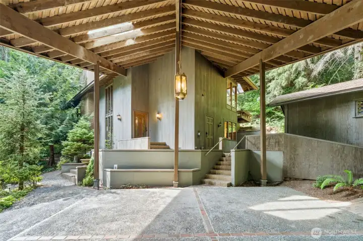 An impressive covered carport showcases bold architectural lines and a striking statement light fixture, providing seamless access to the main entrance along with a convenient ramp designed for effortless accessibility for all.