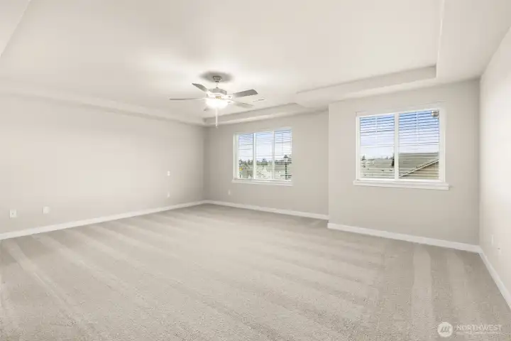 Spacious primary bedroom with carpet flooring creating a soft and calming atmosphere. A ceiling fan with an integrated light fixture is mounted at the center of the ceiling, providing both illumination and airflow.