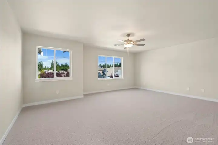 Spacious primary bedroom with carpet flooring creating a soft and calming atmosphere. A ceiling fan with an integrated light fixture is mounted at the center of the ceiling, providing both illumination and airflow.