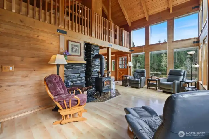 A wall of windows overlooks the lake, filling the space with natural light, while the loft above adds an open view to the main living area and the fireplace ,surrounded by stone, grounds the space.