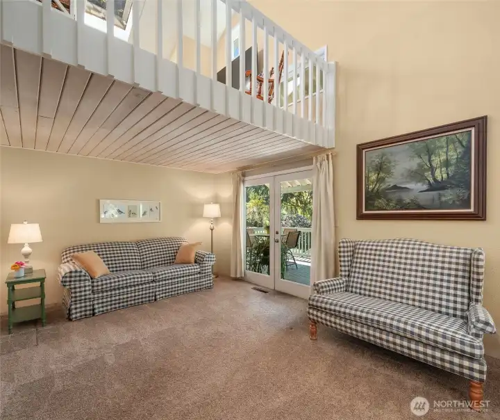 Living room with French doors out to south-facing deck and cozy loft space above.