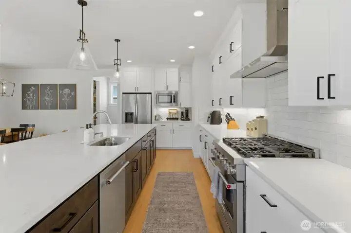 A wide view of the chef's kitchen showcasing the professional-style gas range, stainless hood, and seamless flow into the dining and living spaces. A wide view of the chef's kitchen showcasing the professional-style gas range, stainless hood, and seamless flow into the dining and living spaces.