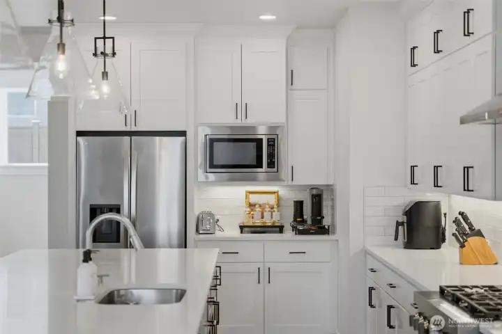 A dedicated coffee and beverage station keeps the main kitchen workflow uncluttered, tucked beside the refrigerator and microwave. A dedicated coffee and beverage station keeps the main kitchen workflow uncluttered, tucked beside the refrigerator and microwave.