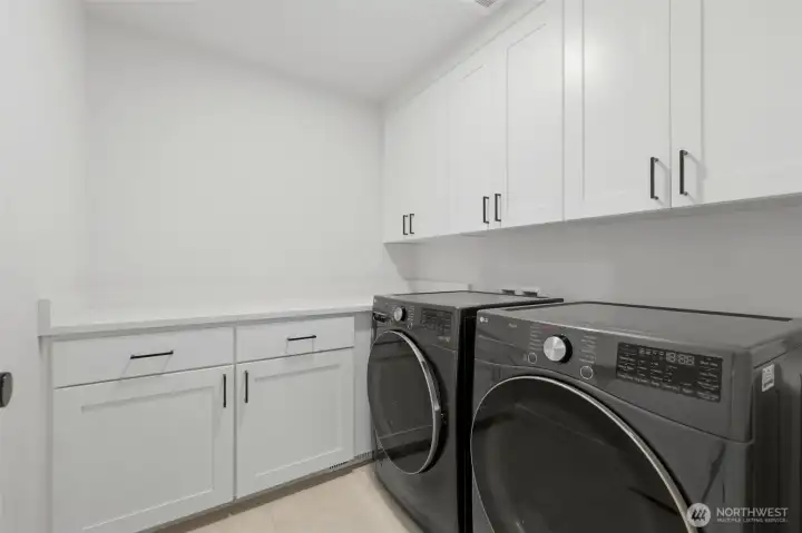 Dedicated laundry room with abundant white cabinetry, quartz folding counter, and full-size LG washer and dryer. Dedicated laundry room with abundant white cabinetry, quartz folding counter, and full-size LG washer and dryer.