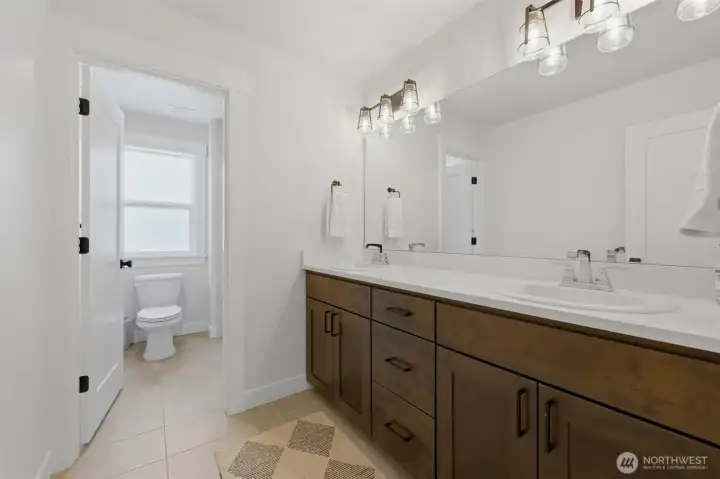 The upstairs hallway bathroom boasts a dual-sink vanity with rich custom cabinetry and quartz countertops, plus a private water closet for added comfort and privacy. The upstairs hallway bathroom boasts a dual-sink vanity with rich custom cabinetry and quartz countertops, plus a private water closet for added comfort and privacy.