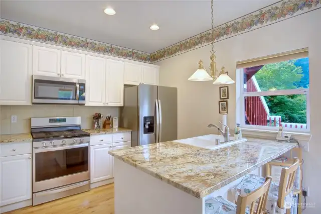 Spacious kitchen with new stainless appliances, gas range, hardwood floors and slab granite countertops. Notice trees and greenery out the window.