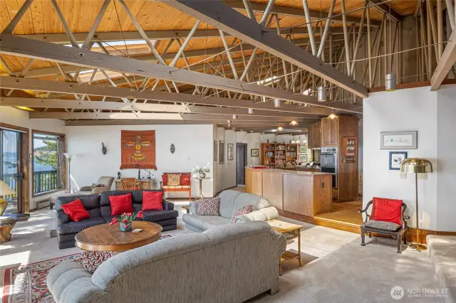 The bright and airy open concept living room, kitchen and dining on the other side of the kitchen. Th door in the back leads to the primary bedroom. The support beams of the structure add an interesting design element to the space.