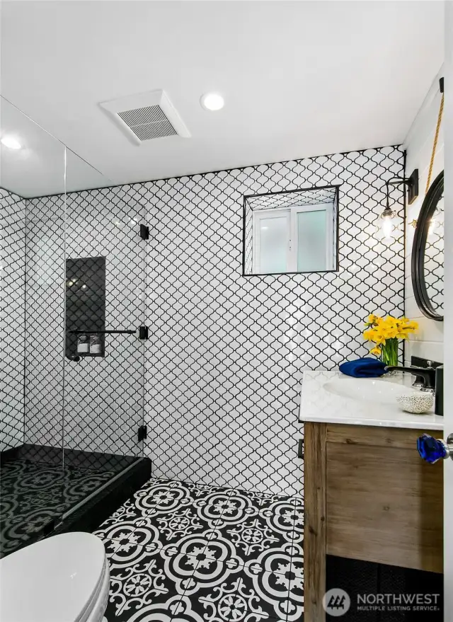Sleek design and artisanal details define this spa-like bath at 7316 Eastside Drive NE. A walk-in shower with frameless glass, striking patterned tilework, and custom finishes elevate everyday routines in the Beach House. Coastal comfort meets curated style.