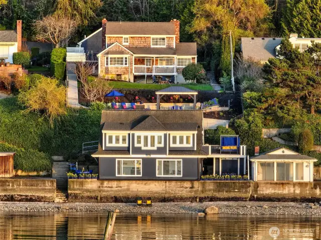 Both 7314 & 7316 Eastside Drive NE are visible in this cinematic shot of Caledonia Cove. At the top: the Cape Cod-style upland residence at 7314. Mid-slope: the versatile Coach House at 7316. Water’s edge: the fully renovated Beach House and petite Boat House, both also part of 7316. Together, these buildings compose a rare street-to-shore estate across two tax parcels.