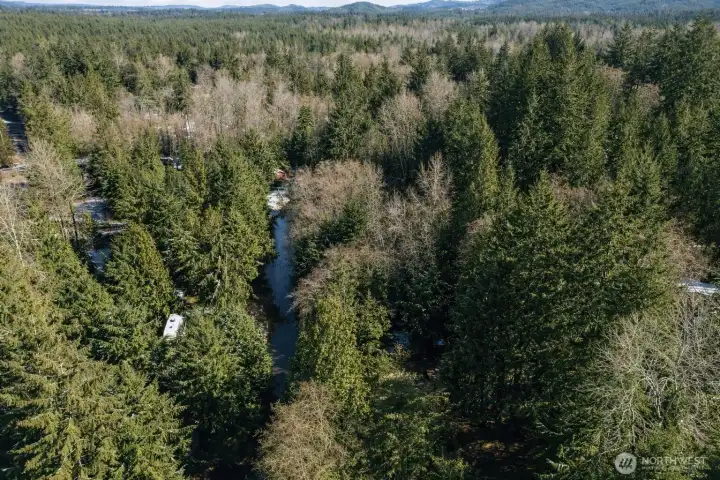 Aerial view showcasing the surrounding forested landscape and scenic waterway, offering privacy and natural beauty.