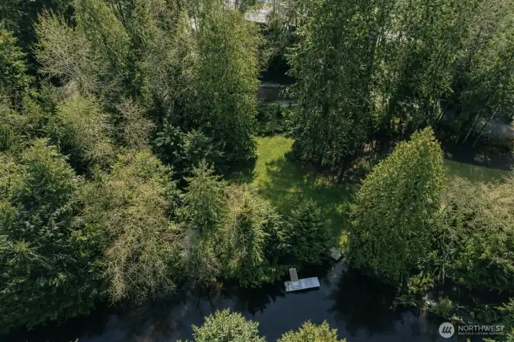 Aerial view highlighting private waterfront access with dock, surrounded by mature trees and lush greenery.