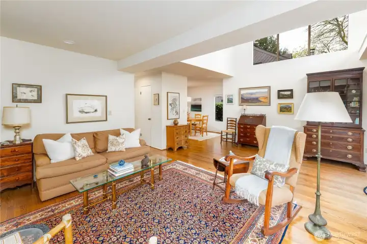 This inviting living room is filled with natural light, highlighted by soaring ceilings and expansive windows that bring the outdoors in. Warm hardwood floors, a cozy seating area, and beautiful built-in details create a comfortable yet refined space that flows seamlessly into the dining area, perfect for both everyday living and entertaining.