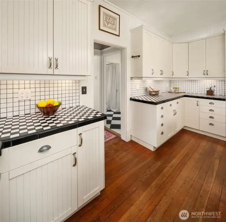 The kitchen respects the period with authentic style cabinetry and tiled countertops. Note the original, gorgeous fir floors throughout the home.