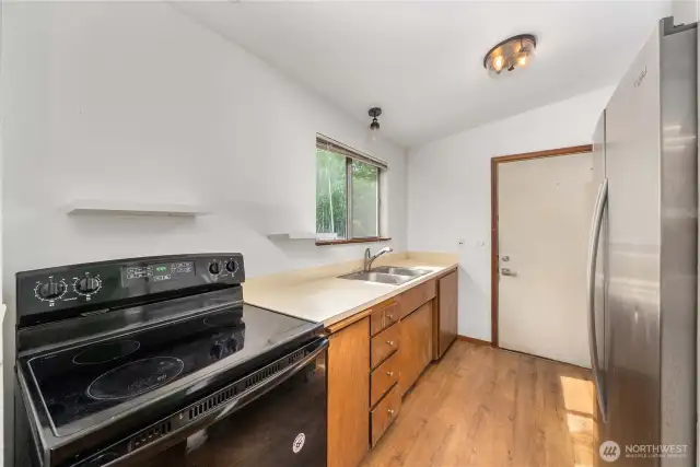 Maximize every inch in this bright galley-style kitchen featuring newer appliances—including a sleek black range and stainless steel fridge. A large window above the sink brings in natural light while offering a peaceful view of the surrounding greenery.
