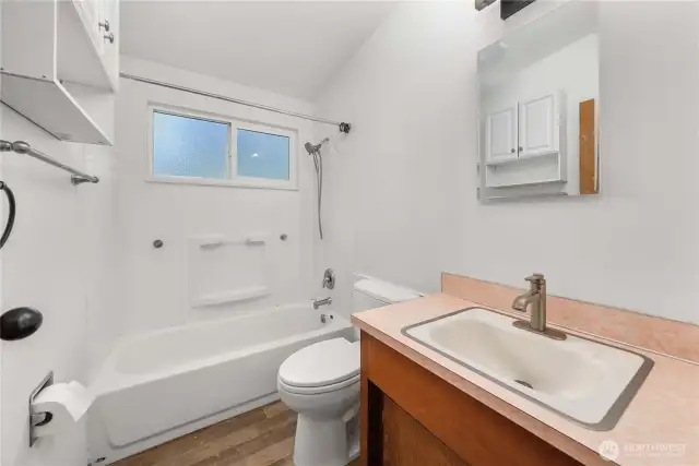 This functional full bathroom features a tub/shower combo, updated faucet, overhead storage, and a large frosted window that brings in soft natural light while maintaining privacy. Simple and efficient with everything you need.