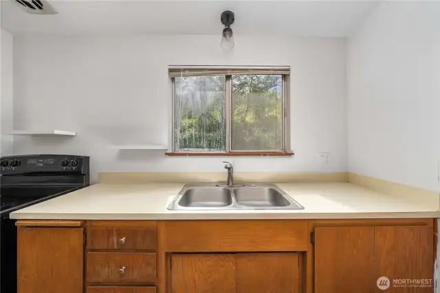 Enjoy peaceful views of the lush, tree-lined backyard while doing dishes at this centrally located double sink. Open shelving adds charm and practicality, while the natural light from the window keeps the space bright and airy.