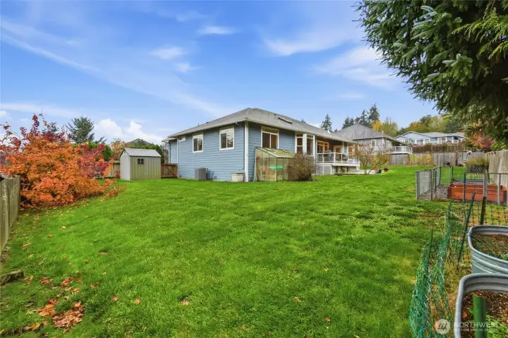 Fully fenced yard with greenhouse and deck for outdoor living.