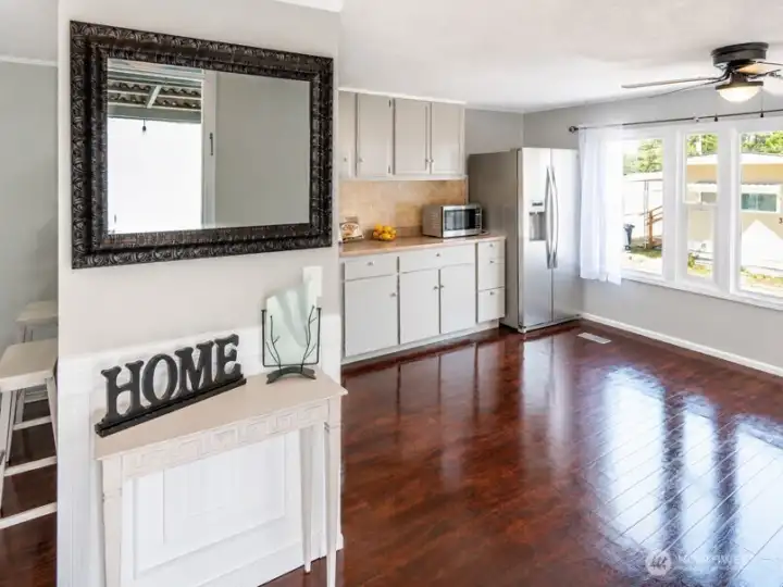 Bright interior entry with hardwood floors, grey cabinetry, and open flow into the kitchen and dining areas.