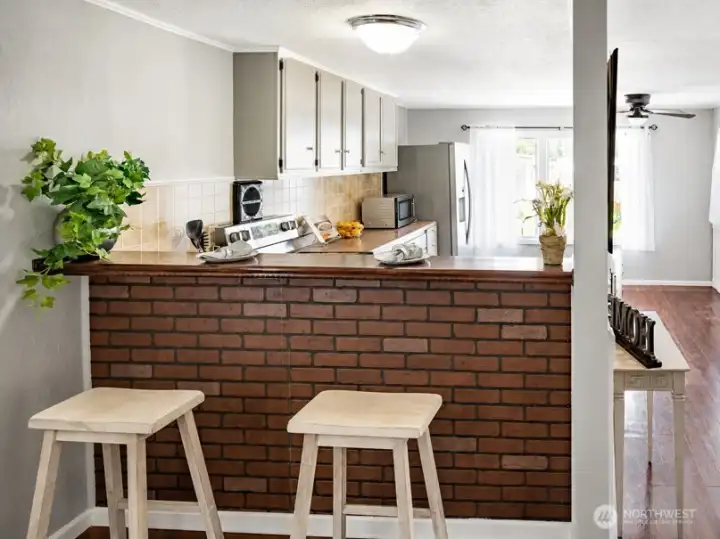 Breakfast bar and kitchen pass-through with brick accent wall, bar seating, and bright adjoining living space.