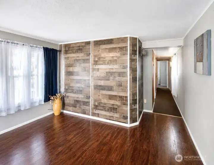 Hallway and living area with hardwood flooring, decorative accent wall, and natural light from large windows.