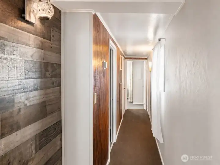 Hallway with accent wall detail, warm wood flooring, and access to adjacent rooms.