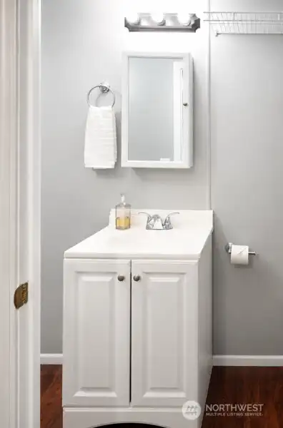 Half-bathroom vanity with white cabinetry, mirror, and clean neutral finishes.