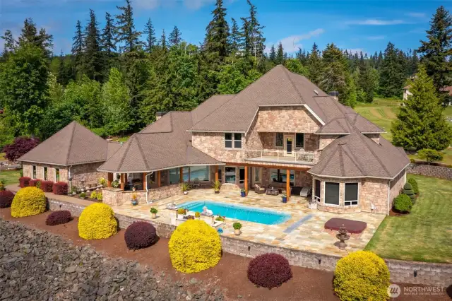 The west-facing side of the home features a slate-tiled pool deck, hot tub, covered seating area, and outdoor kitchen with gas fireplace