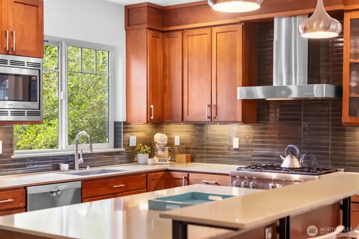 Under-cabinet lighting highlights the glass tile backsplash and quartz counters, with a garden window above the sink bringing in a touch of green.
