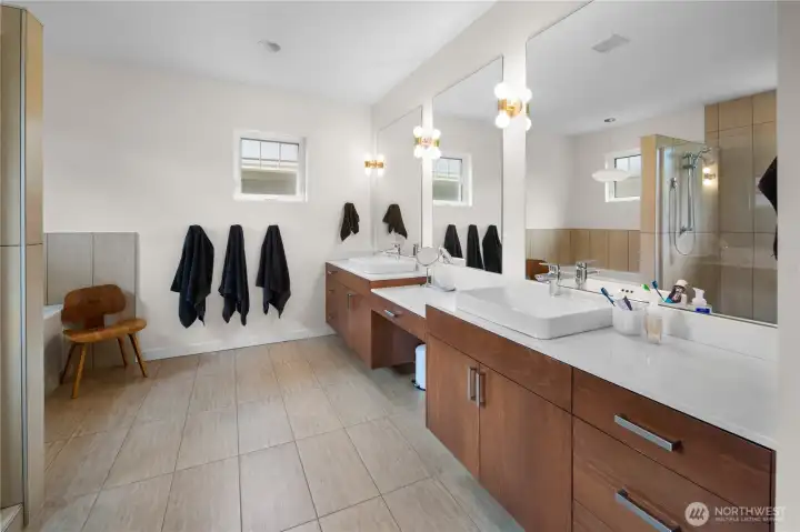 The primary bathroom features a  double-vanity in warm wood with white countertops, a large frameless mirror with globe light sconces, and tilework throughout.