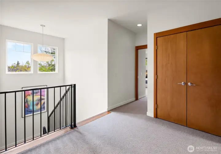 The stair landing opens to the upper level with a saucer pendant, treetop views, and warm wood-trimmed doors leading to the bedrooms beyond.
