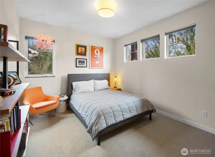 A well-proportioned secondary bedroom with treetop views, built-in shelving, and plenty of room for a desk and seating area alongside the bed.