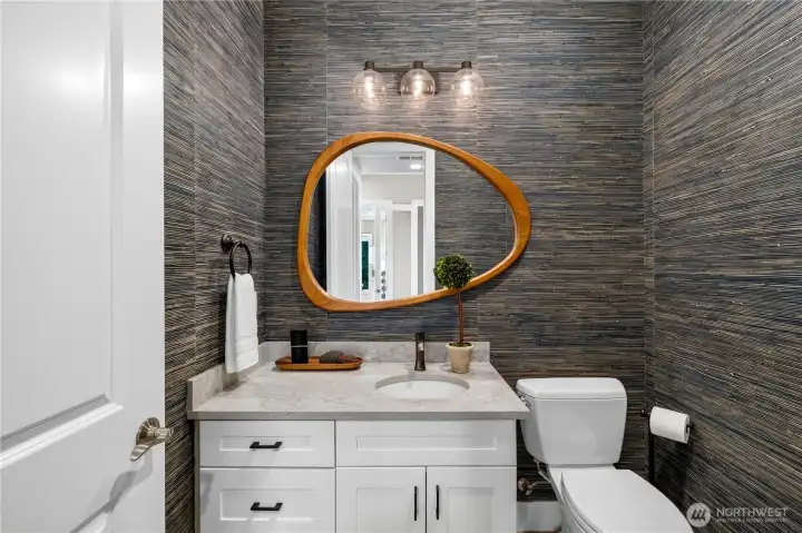 Designer powder room featuring a marble vanity, custom textured wallcovering, sculptural mirror, and curated designer lighting