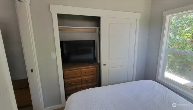 TV nestled in the bedroom closet with dresser and room for hanging clothes.