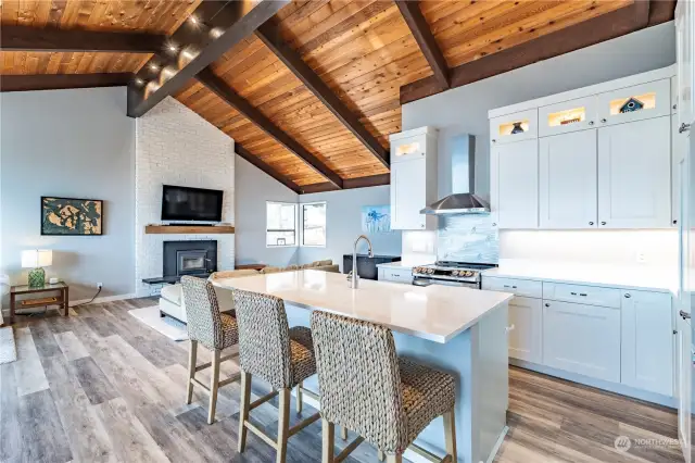 The kitchen has an eating bar, quartz countertops, stainless steel appliances, lovely cabinet lighting and a custom backsplash at the range/oven.