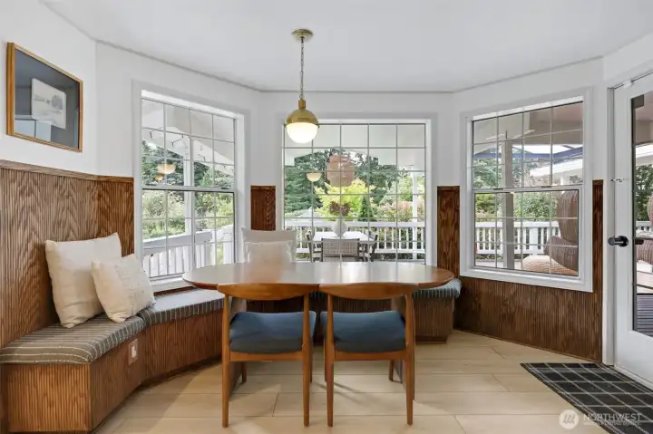 A warm and inviting eating nook with built-in seating, surrounded by windows that fill the space with natural light—complete with a door to the right for easy access to the covered deck.