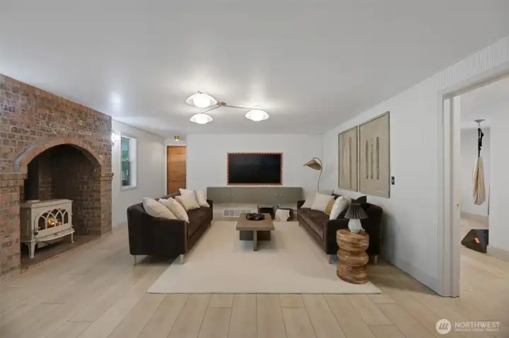 Spacious family room anchored by a cozy gas fireplace, offering a warm and inviting gathering space. In the distance, a door leads to the garage, with a secondary staircase to the upper level just to the right. Closer in, an additional door provides access to the versatile main-level bonus room.