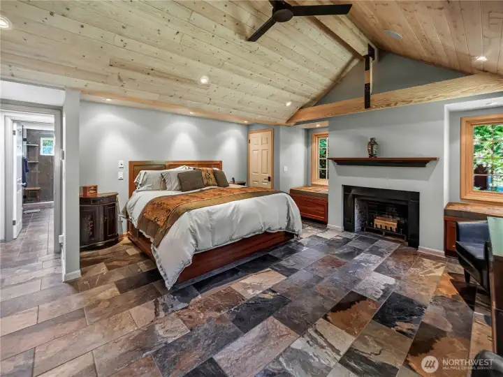 Primary bedroom with vaulted ceilings, heated tile floors, & a wood fireplace.