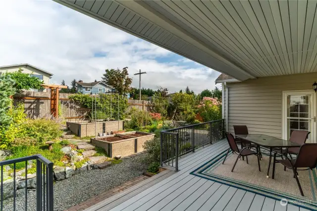 Large covered backyard deck with with a private door to the primary private bedroom, sliding glass door to the dining and kitchen area. Also the owners built wood arbor in the distance! The deck rug, chairs and glass table stay with the house.