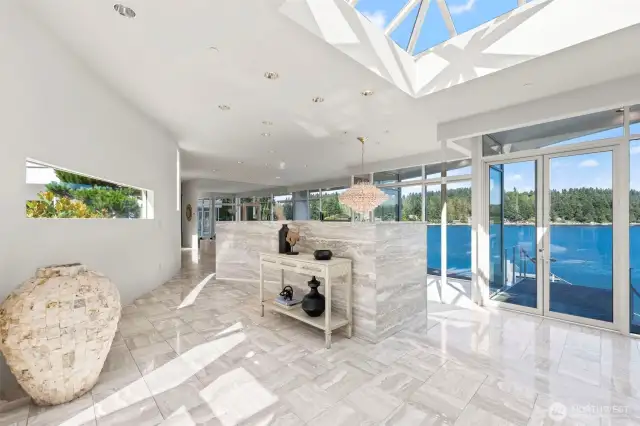 Step inside to a sunlit foyer where marble floors, sculptural lines, and expansive glass immediately frame Wollochet Bay’s blue expanse — a striking prelude to this architectural icon