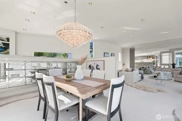Positioned to capture both natural light and serene bay views, the dining space blends elegance with function. A sculptural crystal chandelier makes a statement overhead, while built-in glass display cabinetry adds a sleek, modern touch. Flowing seamlessly from the living room, this open-concept design is perfect for entertaining, offering a refined setting for intimate dinners or lively gatherings—all while showcasing the home’s distinctive waterfront architecture.