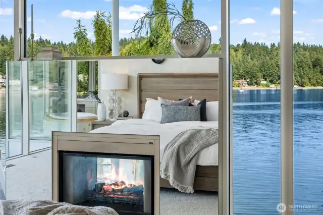 A see-through fireplace and walls of glass connect the primary suite to sweeping waterfront views, blending cozy warmth with an awe-inspiring natural backdrop.
