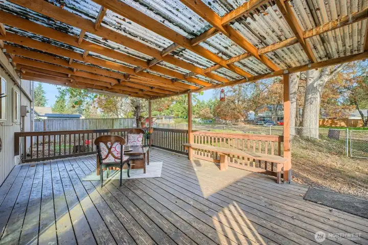 Large covered deck with built-in seating & wood railings. Chicken coop area partitioned in the distance/corner of yard