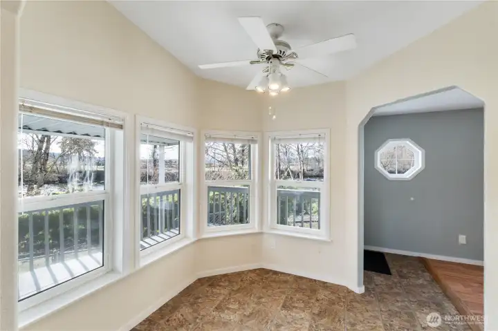 A window-wrapped breakfast nook filled with natural light, overlooking a gently flowing river. The warm, cozy space invites quiet mornings with coffee and a good book.