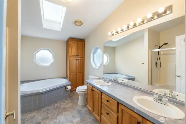 Light-filled primary bathroom with skylight, soaking tub, walk-in shower, and dual sinks.