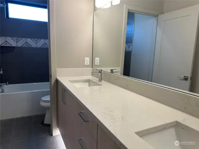 Large guest bathroom with double vanity, quartz counters, tub/shower with tiled walls, window and motion activated toe-kick lighting.