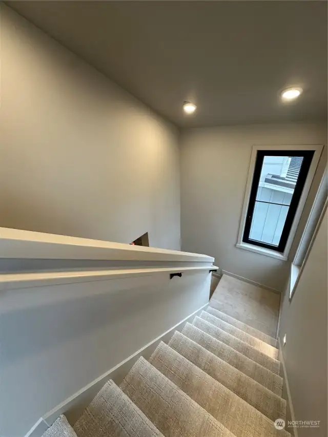 View of the open stairwell with windows for beautiful lighting and warm neutral color tones.