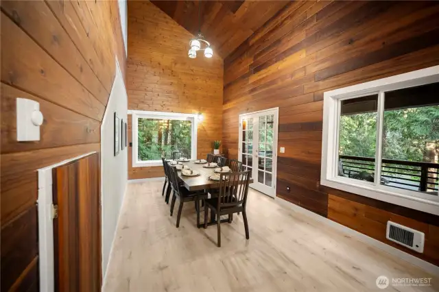 Stunning dining room with soaring wood-paneled ceilings, abundant natural light, and beautiful forest views-fun game nook closet to the left of the photo.